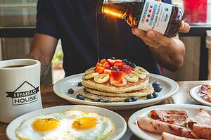 man pouring maple syrup on pancakes at breakfast restaurant